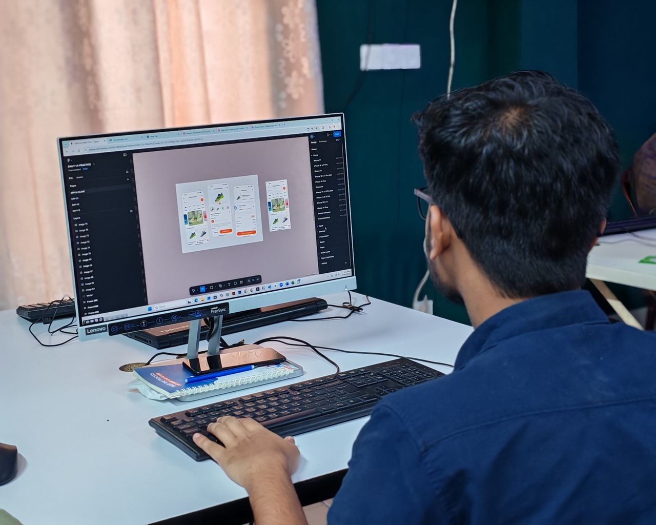 A young designer focused on creating user interfaces on a desktop computer in an office setting.